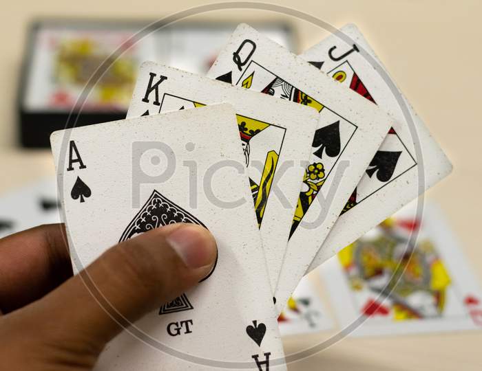A hand holding ace, jack, queen, king of spades playing cards