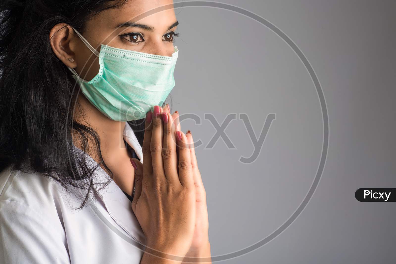 Young Woman Doctor Doing Namaste Because Of Outbreak Of Covid-19. New Greeting To Avoid The Spread Of Coronavirus Instead Of Greeting With A Hug Or Handshake.