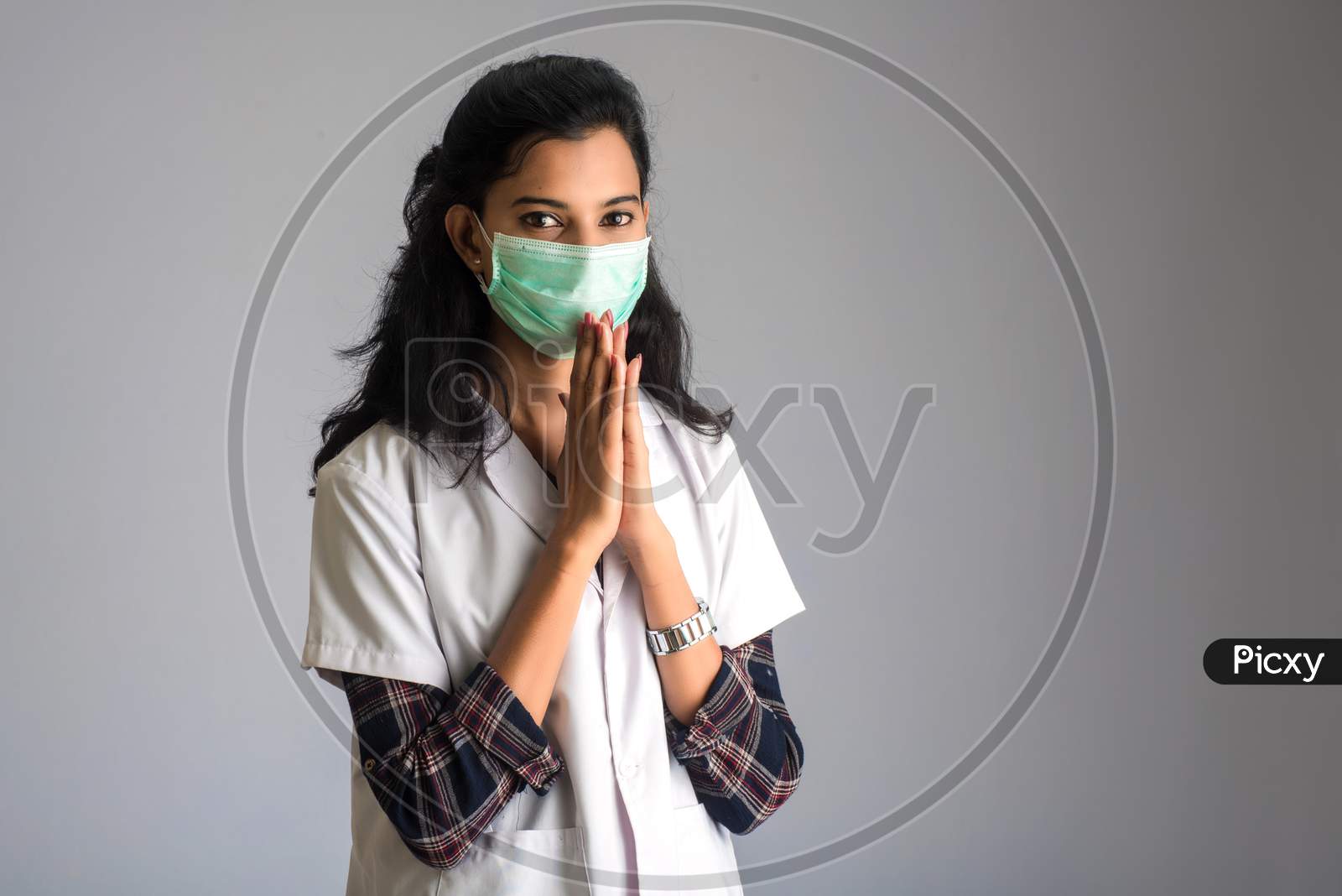 Young Woman Doctor Doing Namaste Because Of Outbreak Of Covid-19. New Greeting To Avoid The Spread Of Coronavirus Instead Of Greeting With A Hug Or Handshake.