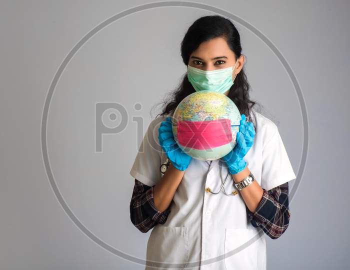 Woman Doctor Holding World Globe With A Medicine Face Mask. World Epidemic Of Coronavirus Concept.
