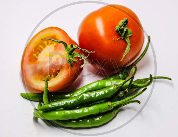 Green Chillies And Tomato Over An Isolated White Background