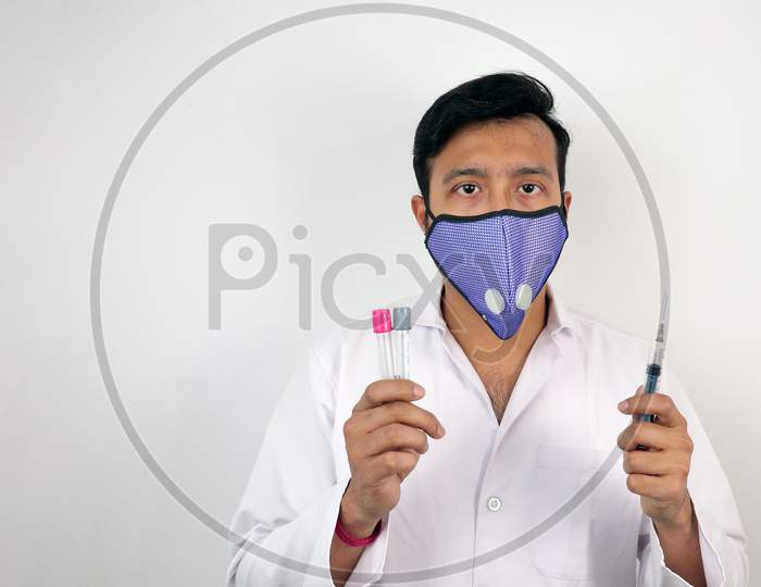 a medical professional in white coat and protective mask holding syringe in hand.