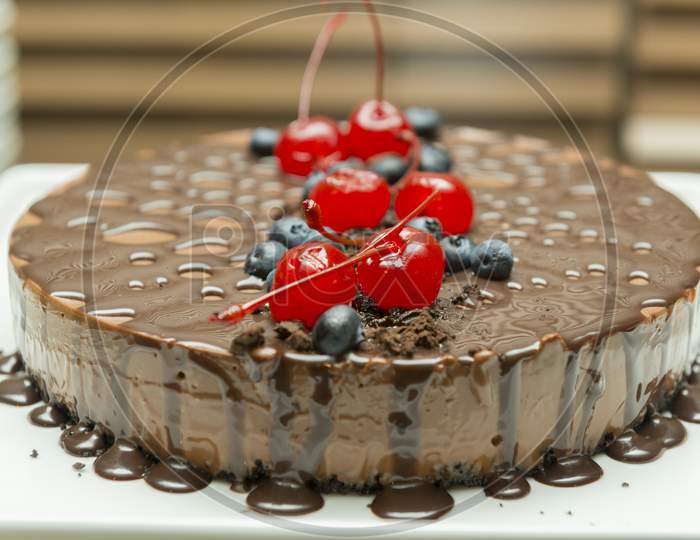 Beautiful And Tasty Chocolate Dessert, With Syrup And Cherry And Blueberry Topping. Delicious Chocolate Pie On White Platter. Gourmet Food Concept. Selective Focus.