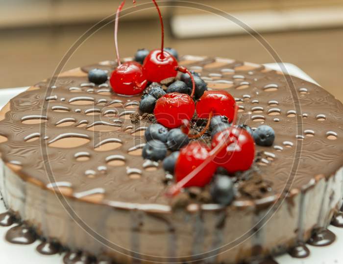 Beautiful And Tasty Chocolate Dessert, With Syrup And Cherry And Blueberry Topping. Delicious Chocolate Pie On White Platter. Gourmet Food Concept. Selective Focus.