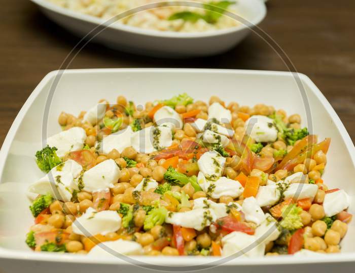 Closeup Of Chickpea Salad With Tomatoes, Broccoli And Buffalo Cheese On A Foursquare Ceramic Platter On Wooden Table. Healthy And Tasty Food. Selective Focus.
