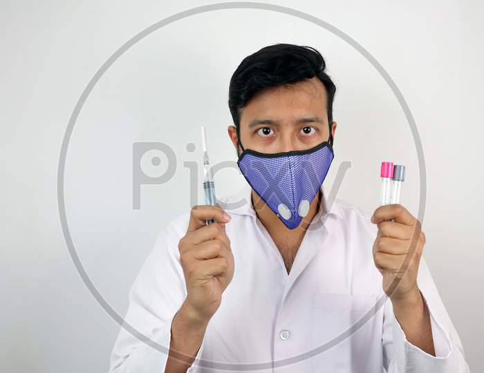 a medical professional in white coat and protective mask holding syringe in hand.