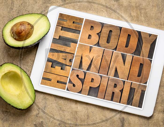 Health, Body, Mind And Spirit Word Abstract In Vintage Wood Letterpress Wood Type On A Digital Tablet With Avocado, Holistic Approach To Wellbeing Concept