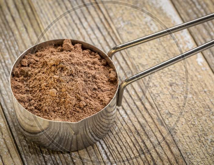 Cacao Powder In A Metal Measuring Scoop Against Grunge Wood Background