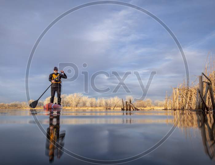 Senior Male Paddler In A Wetsuit Is Paddling A Stand Up Paddleboard On A Lake In Colorado, Winter Or Early Spring Scenery, Low Angle Action Camera View, Recreation, Fitness And Training Concept
