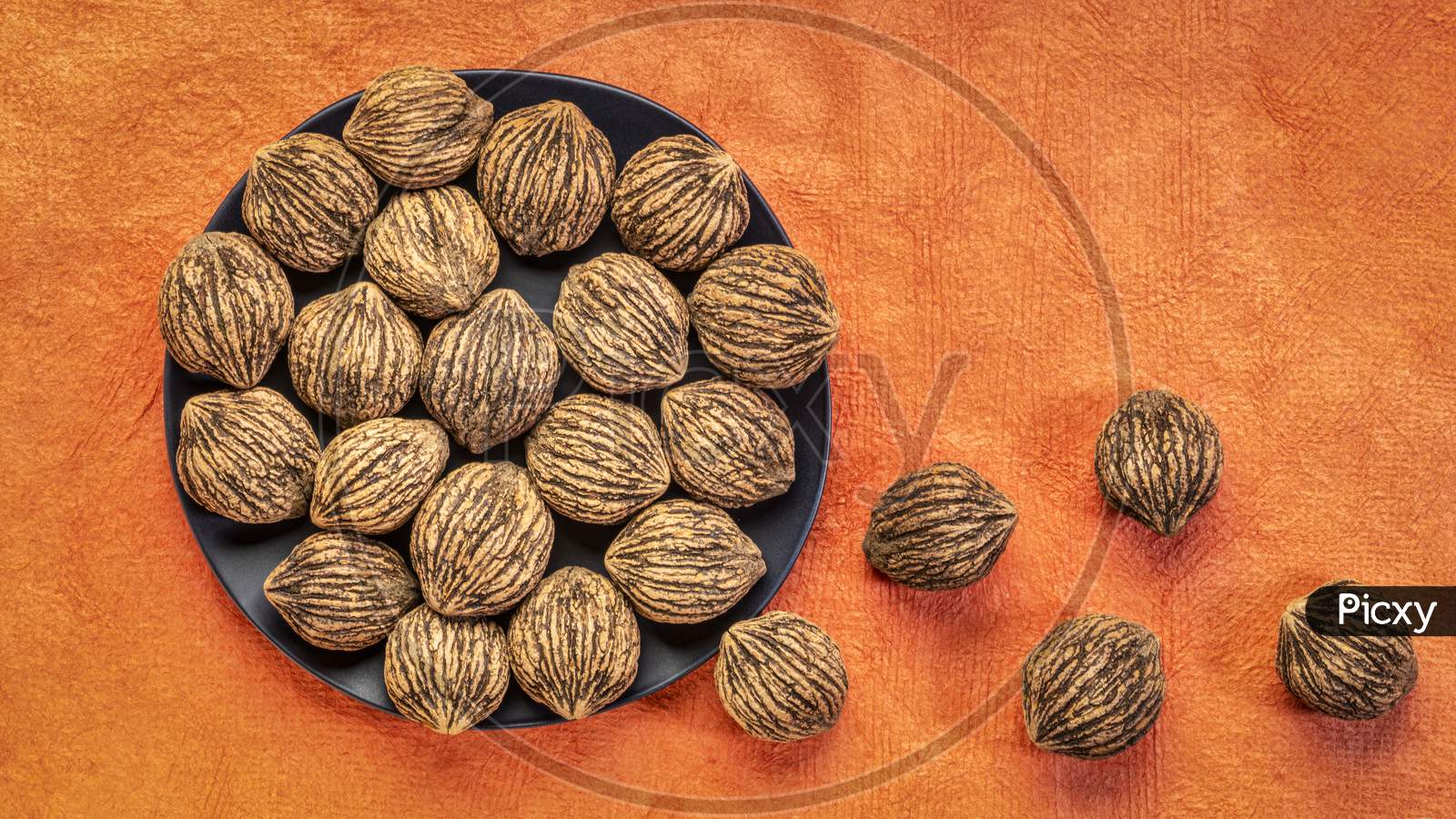 Black Walnuts On A Black Plate And Orange Textured Paper Background With A Copy Space