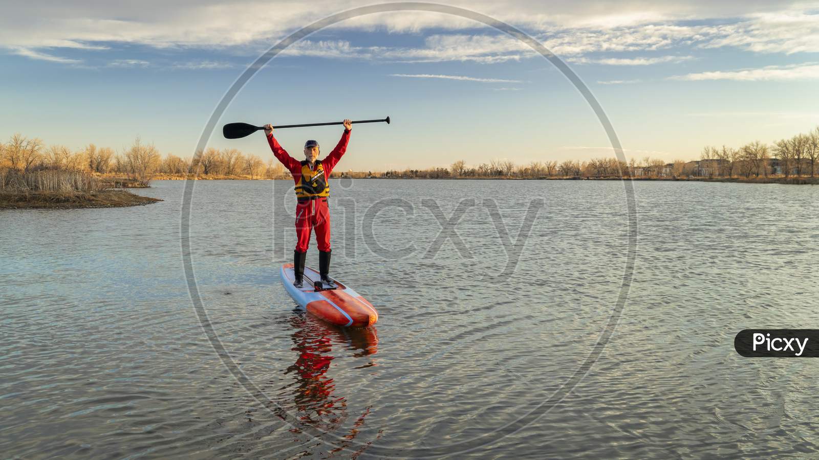 Senior Male Paddler In A Drysuit And Life Jacket Is Paddling A Long Racing Stand Up Paddleboard On A Lake In Colorado, Winter Or Early Spring Scenery, Recreation, Fitness And Training Concept