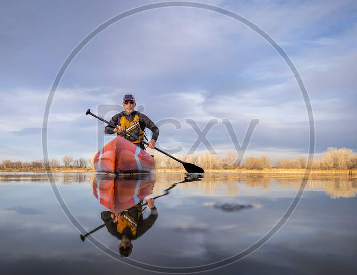 Senior Male Paddler In A Wetsuit Is Paddling A Stand Up Paddleboard On A Calm Lake In Colorado, Winter Or Early Spring Scenery, Low Angle Action Camera View, Recreation, Fitness And Training Concept