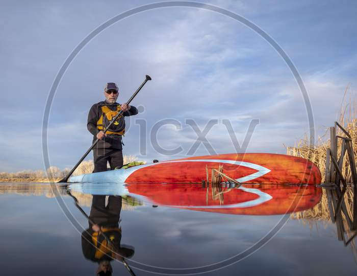Senior Male Paddler In A Wetsuit Is Paddling A Stand Up Paddleboard On A Lake In Colorado, Winter Or Early Spring Scenery, Low Angle Action Camera View, Recreation, Fitness And Training Concept