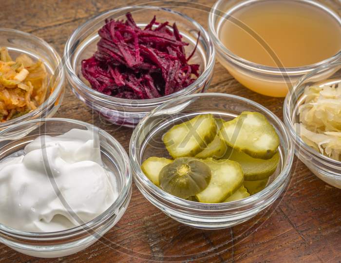 A Sampler Of Fermented, Prebiotics, Food Great For Gut Health - Glass Bowls Against Wood:  Kimchi, Red Beets, Apple Cider Vinegar, Coconut Milk Yogurt, Cucumber Pickles, Sauerkraut