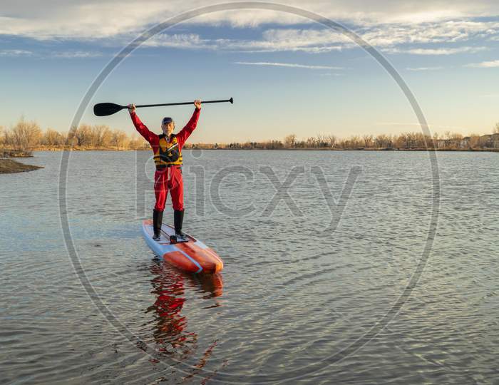 Senior Male Paddler In A Drysuit And Life Jacket Is Paddling A Long Racing Stand Up Paddleboard On A Lake In Colorado, Winter Or Early Spring Scenery, Recreation, Fitness And Training Concept