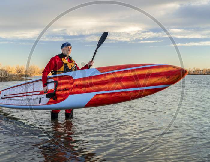 Senior Male Paddler In A Drysuit And Life Jacket Is Finishing His Workout With A Long Racing Stand Up Paddleboard On A Lake In Colorado, Winter Or Early Spring Scenery, Recreation, Fitness And Training Concept