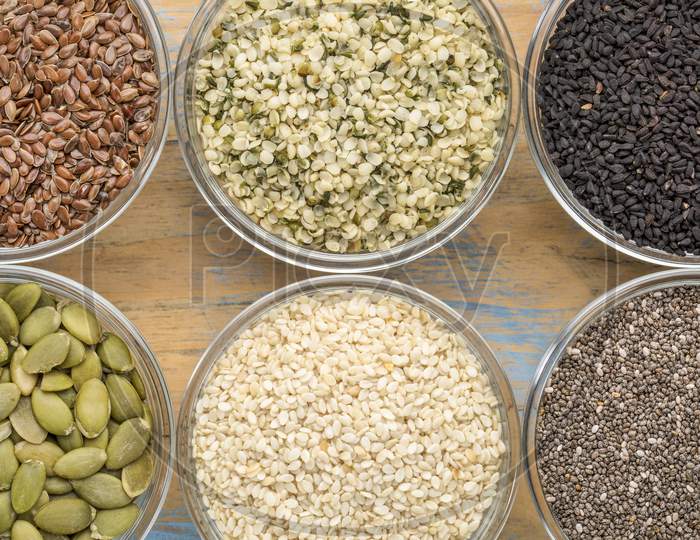 Healthy Seed Collection (Chia, Hemp Hearts, Brown Flax, Pumpkin, Black Cumin, White Sesame) - Top View Of Small Glass Bowls Against Grunge Wood