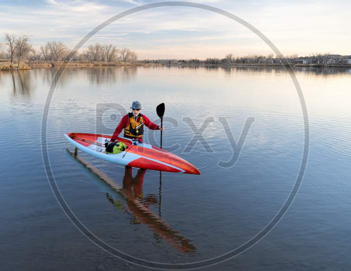 Senior Male Paddler In A Drysuit And Life Jacket Is Finishing His Workout With A Long Racing Stand Up Paddleboard On A Lake In Colorado, Winter Or Early Spring Scenery, Recreation, Fitness And Training Concept