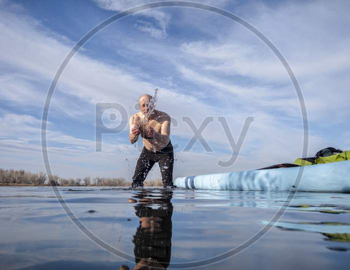 Senior Male Paddler Is Rinsing And Splashing Himself In Icy Lake Water After Workout On A Stand Up Paddleboard, Lake In Colorado, Winter Or Early Spring Scenery, Recreation, Fitness And Training Concept