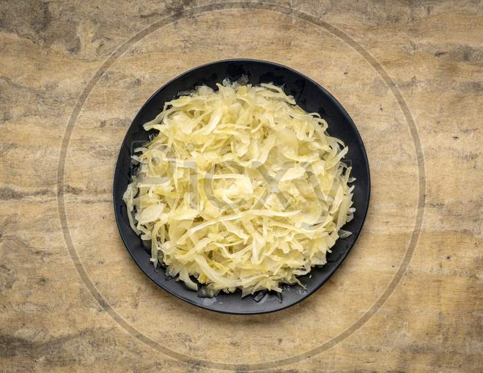 Black Plate Of Sauerkraut Against  Bark Textured Paper Background, Prebiotics Concept - Fermented Food Good For Gut Health