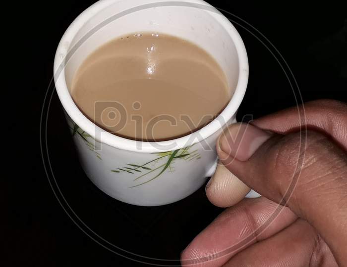 A guy is holding tea cup in his hand in black background