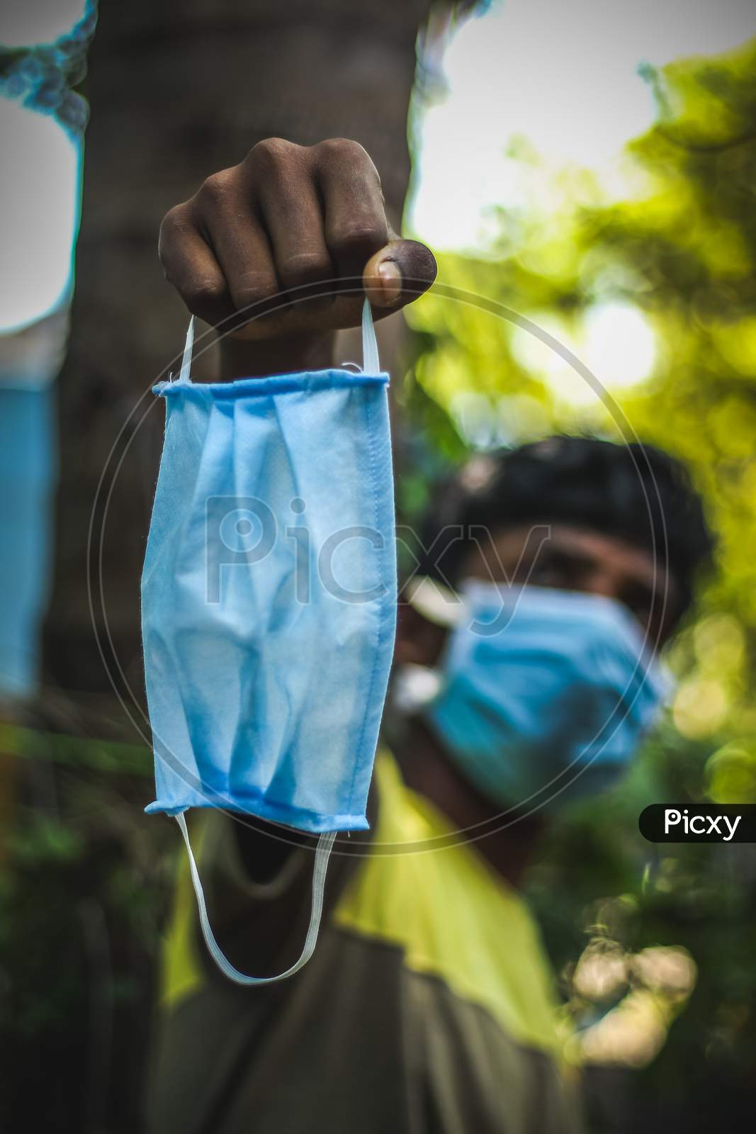 Protection Against Contagious Disease, Coronavirus. Man Wearing Hygienic Mask And Holding On His Hand To Prevent Infection, Airborne Respiratory Illness Such As Flu, 2020. Outdoor Shot Isolated On Nature Background. Asian Young Man Wearing Blue Mask