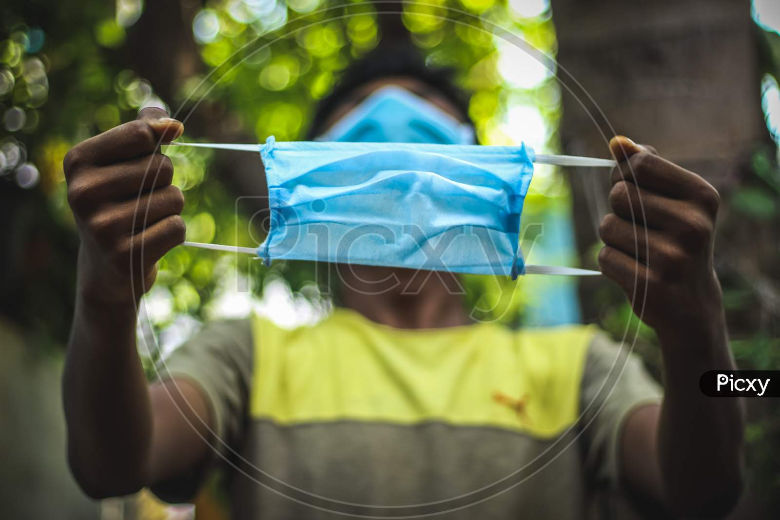 Protection Against Contagious Disease, Coronavirus. Man Wearing Hygienic Mask And Holding On His Hand To Prevent Infection, Airborne Respiratory Illness Such As Flu, 2020. Outdoor Shot Isolated On Nature Background. Asian Young Man Wearing Blue Mask