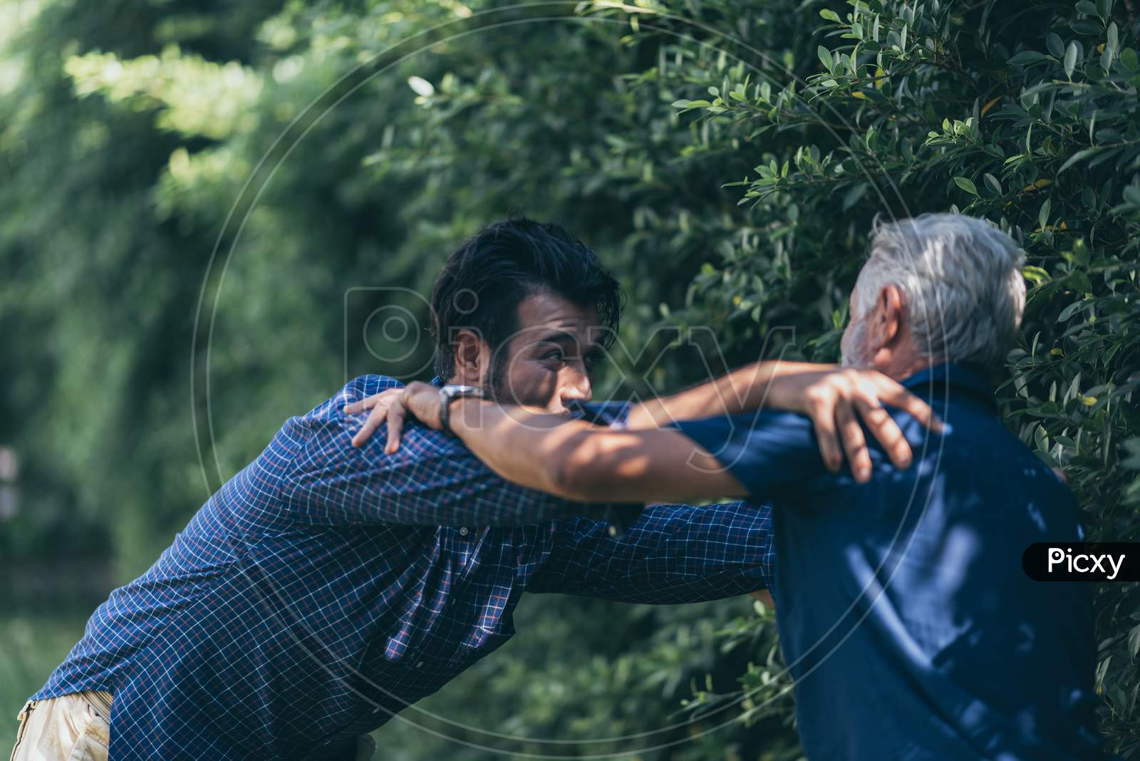 The Old Man And His Son Are Walking In The Park. A Man Hugs His Elderly Father. They Are Happy And Smiling