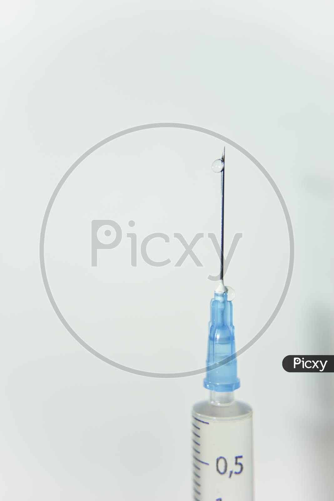 Clear Drop Of The Vaccine On The Top Of The Needle Of Syringe On The White Background