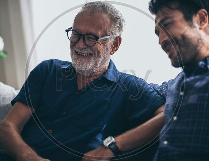 Sweet Bonding. Cheerful Elderly Man Sitting On The Sofa Next To His Adult Son, Hugging Him And Posing Together With Him