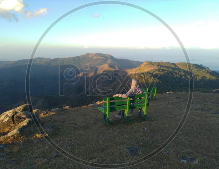 A man with hoodie watching sunrise from the top of the mountain.