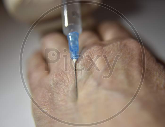 Hand In The Medical Glove With Syringe Prepared To Make An Injection Into Wrinkled Hand On The White Background