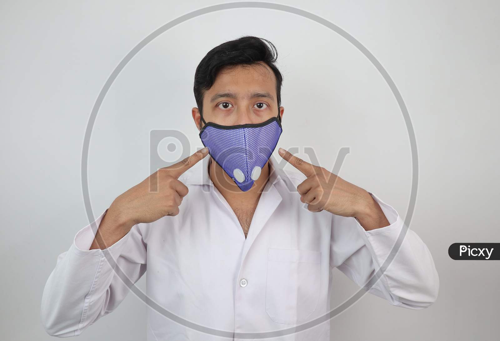 A Medical Professional In White Coat And N 99 Mask Pointing Towards The Mask In White Background With Space For Text.