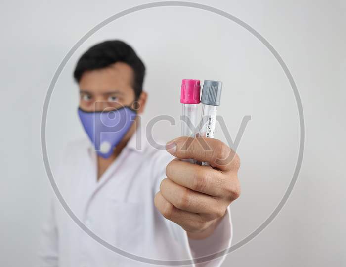 A Medical Professional In White Coat And N 99 Mask With Vials In Hand In White Background With Space For Text.