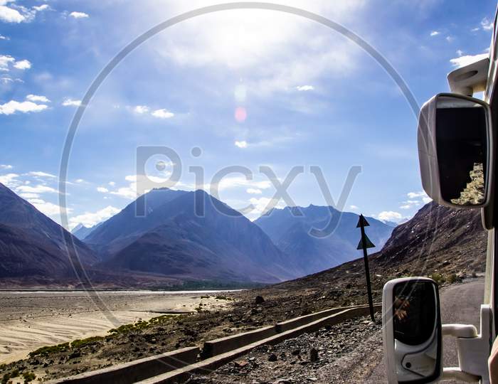 View Of Roads Of Ladakh Kashmir From Car Window While Travelling In A Car With Hills And Blue Sky.