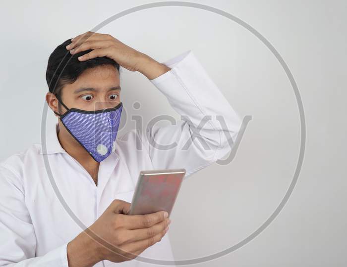 A Male Doctor With Mask And White Coat Shocked To See A News In His Mobile Phone In Hand Isolated In White Grey Background With Copy Space For Text