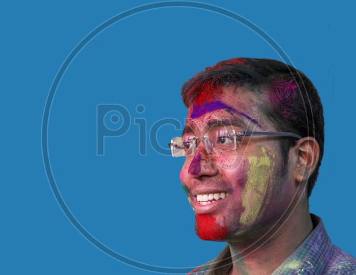 Side Portrait Of A Young Man With Holi Colours On Face Smiling A With Isolated Solid Sky Background.