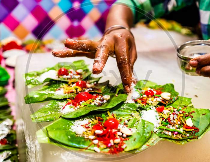 A Hand Sprinkling Pan Masala Garnish And Cherry On Betel Leaf During Preparation Of Banarasi Pan