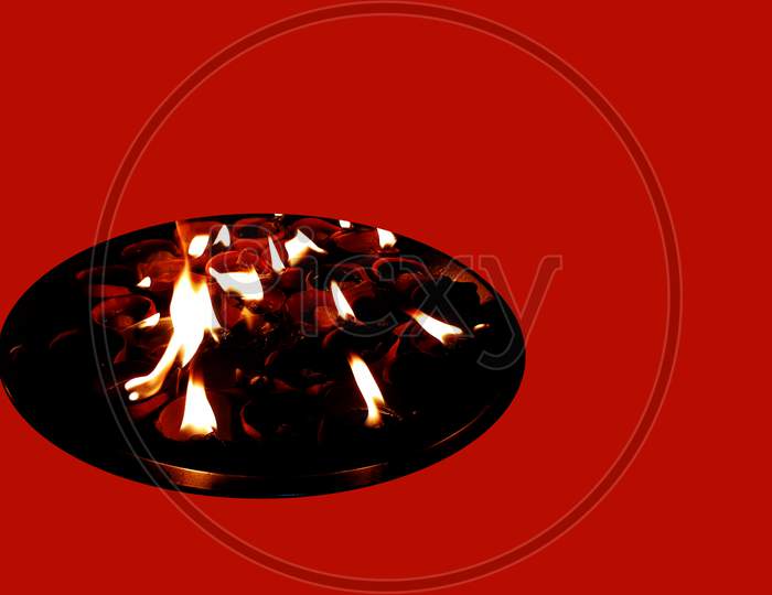 Collection Of Burning Earthen Oil Lamps On A Steel Plate In A Red Background With Copy Space