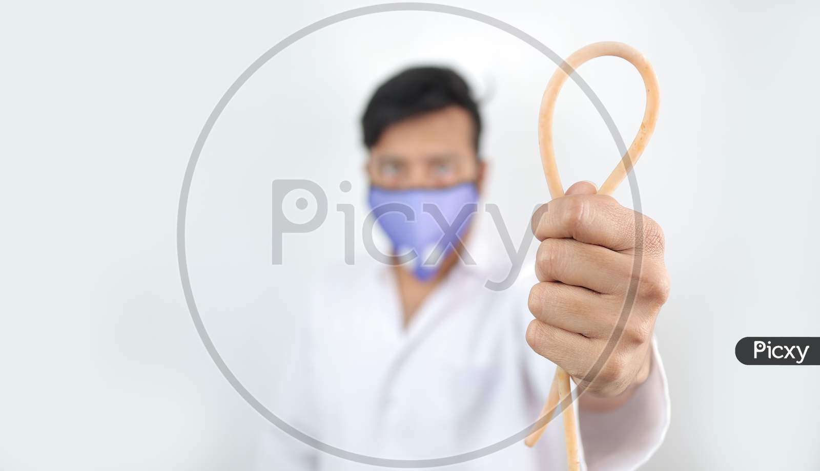 A Medical Professional In White Coat And Protective Mask Holding A Tourniquet In Hand With Selective Focus In Hand With Blurred Background.