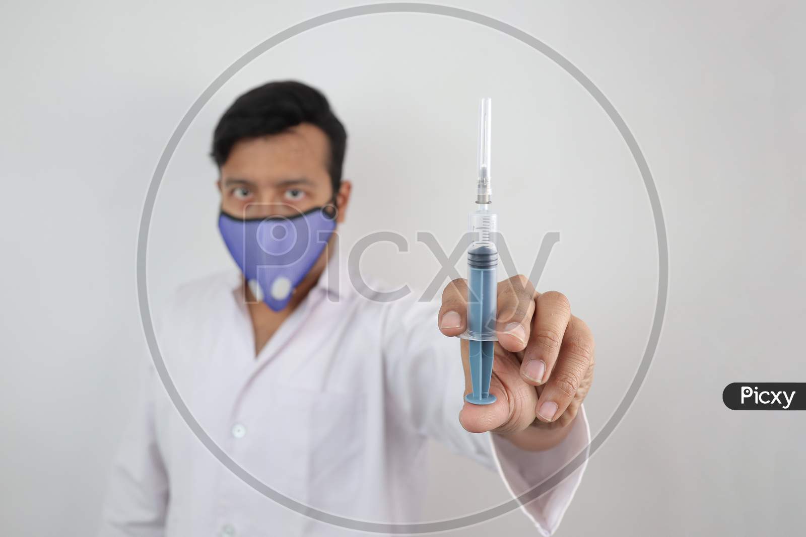 A Medical Professional In White Coat And N 99 Mask With A Syringe In Hand In White Background With Space For Text.