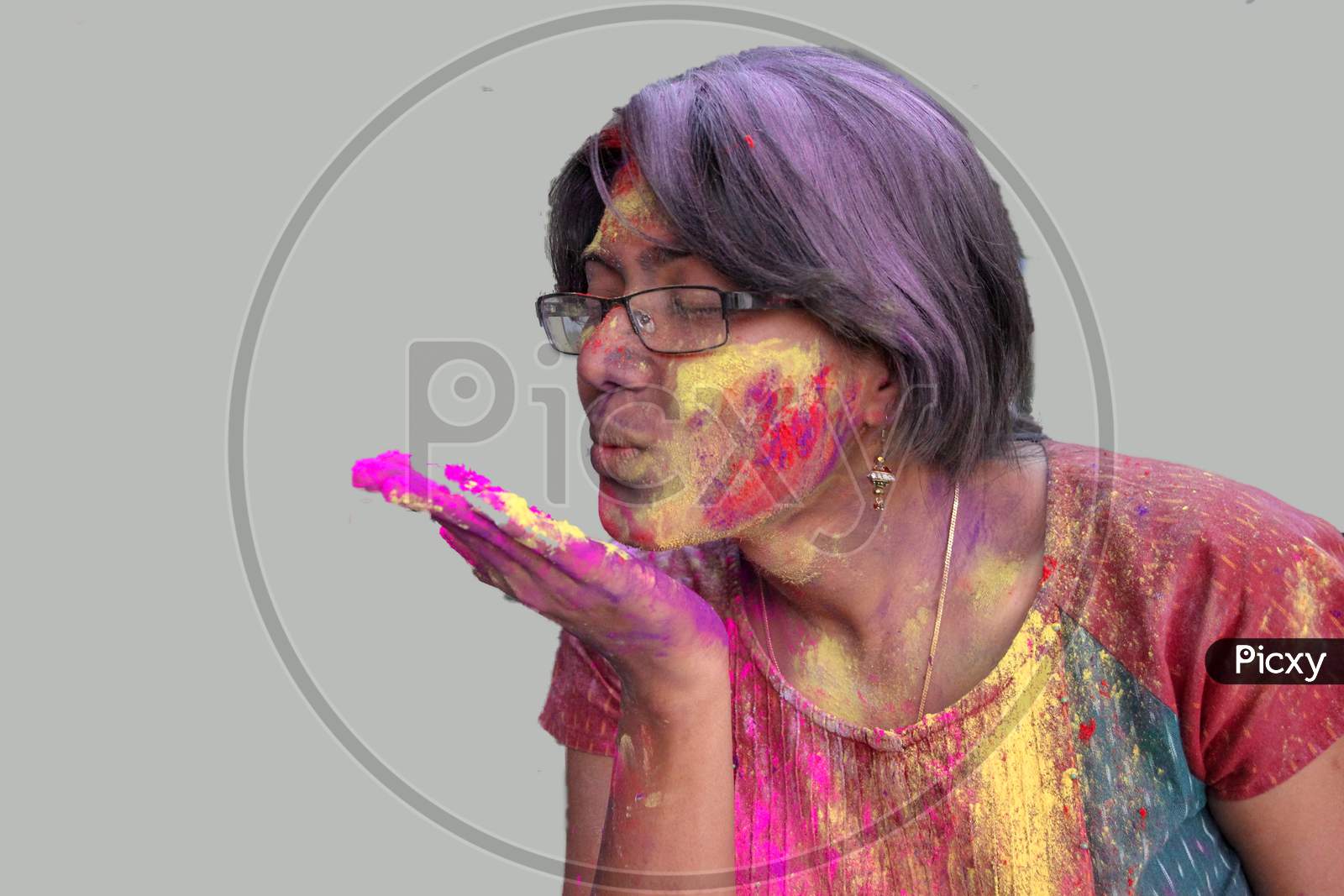Portrait Of A Young Lady With Holi Colours On Face Blowing A Flying Kiss With Isolated Solid Grey Background.