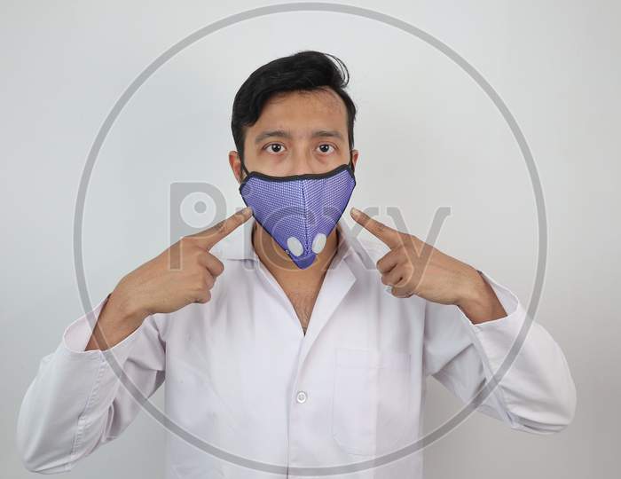 A Medical Professional In White Coat And N 99 Mask Pointing Towards The Mask In White Background With Space For Text.