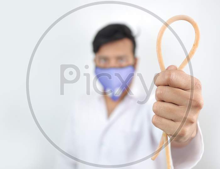 A Medical Professional In White Coat And Protective Mask Holding A Tourniquet In Hand With Selective Focus In Hand With Blurred Background.