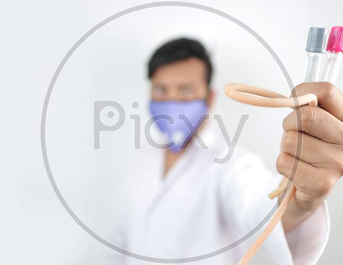 A Medical Professional In White Coat And Protective Mask Holding Vials And Tourniquet In Hand With Selective Focus In Hand With Blurred Background.