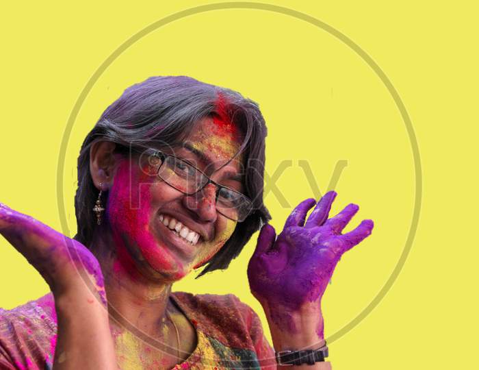 Portrait Of A Young Lady With Holi Colours On Face Smiling At The Camera With Isolated Solid Yellow Background.