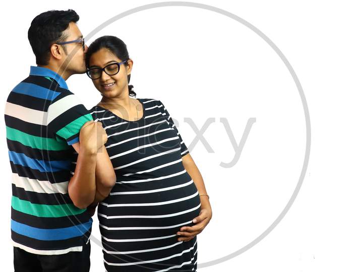 A Young Couple Showing A Pregnant Lady In Satisfied Content Expression With Her Husband Kissing Ger Head In White Background With Copy For Text.