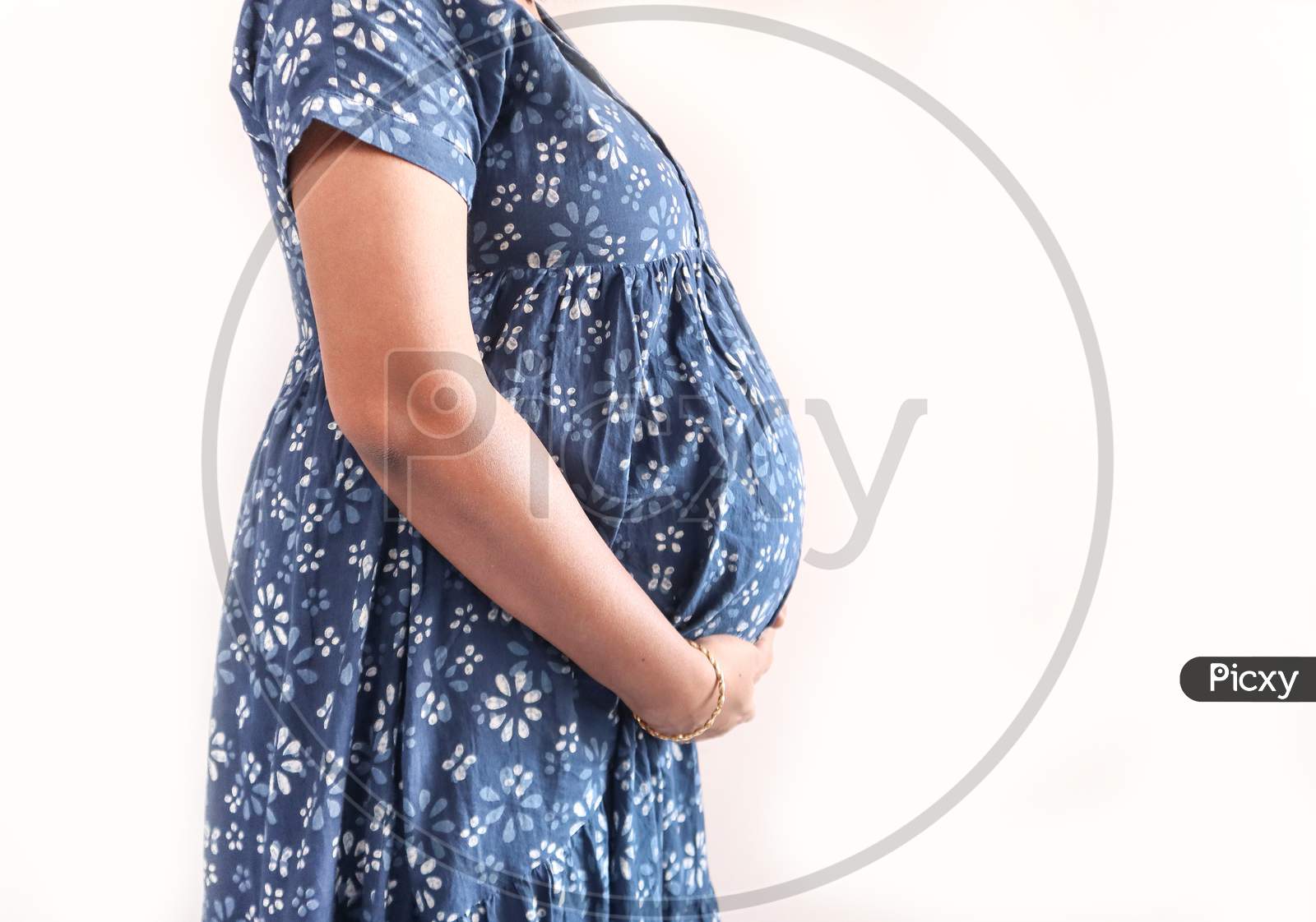 A Pregnant Lady With Blue Dress And Hands On Belly