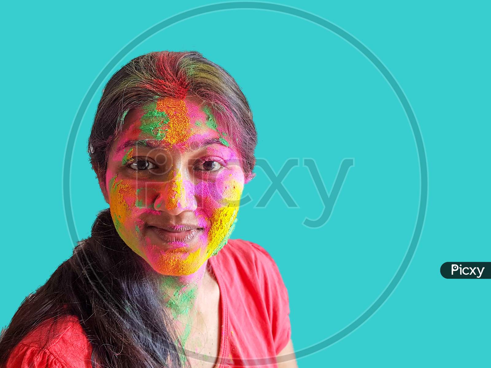 Portrait Of A Young Lady With Holi Colours Smiling At The Camera With Isolated Solid Cyan Background.