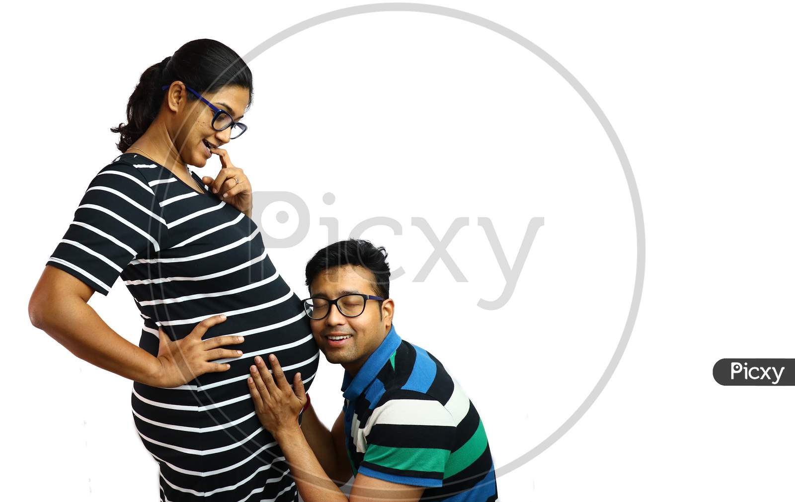 A Young Couple Showing A Pregnant Lady In Inquisitive Expression With Her Husband Placing Ear On Her Belly In White Background With Copy For Text,